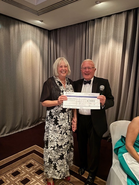 A woman and a man stand holding a large cheque